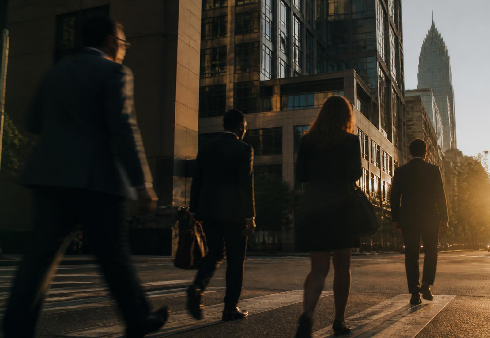 Professionals crossing an uptown Charlotte street at golden hour beneath modern office architecture